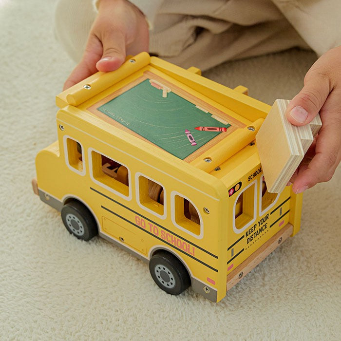 Child's hand pushing wooden school bus with character figure seated in driver's seat behind steering wheel