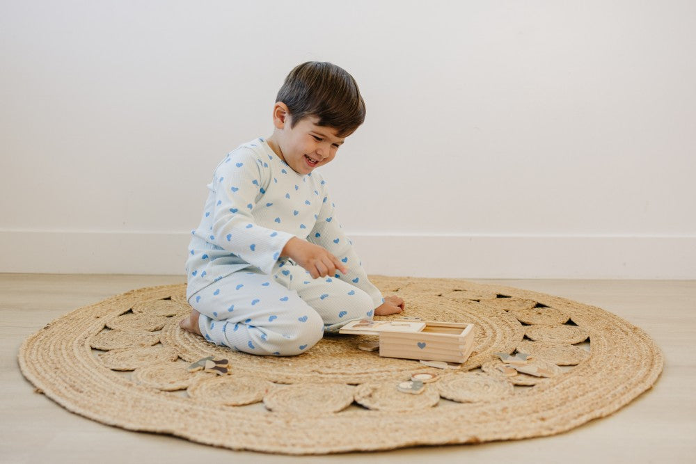 Child playing with a wooden toy on a round jute rug in a minimalistic room.