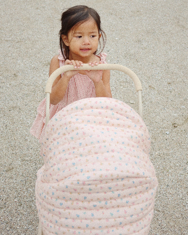 Soft pink and floral pattern doll pram with four spoked wheels and romantic quilted fabric details