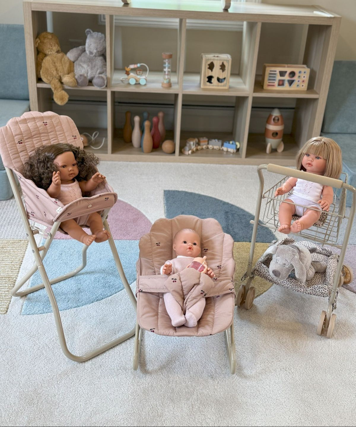 Three dolls in a playroom setting with toys and furniture.