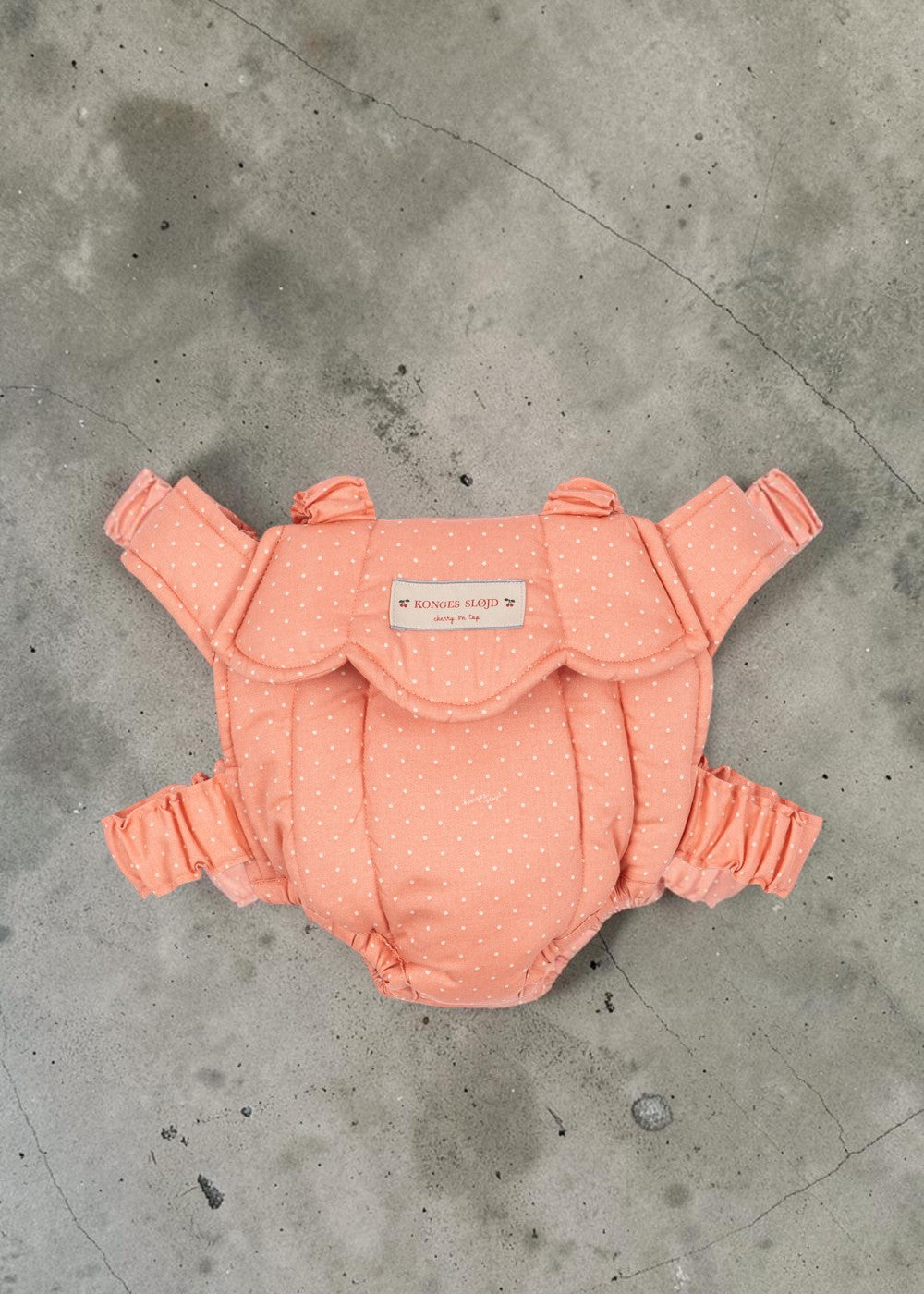 Playroom Collective Konges Sloejd baby doll carrier in coral pink with white dots and scalloped edge detail.