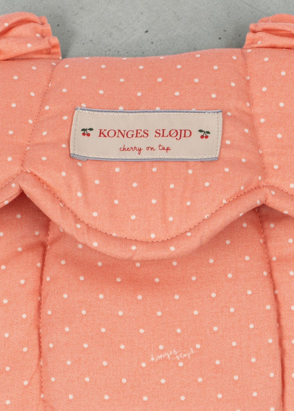 Playroom Collective Konges Sloejd baby doll carrier in coral rose dot cotton with a scalloped edge and brand label.