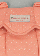 Playroom Collective Konges Sloejd baby doll carrier in coral rose dot cotton with a scalloped edge and brand label.