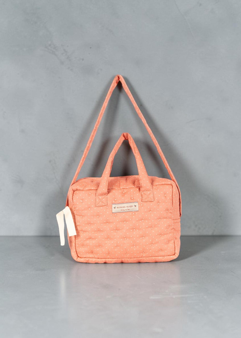 Playroom Collective Konges Sloejd doll diaper bag in coral cotton with white dot pattern and adjustable strap.