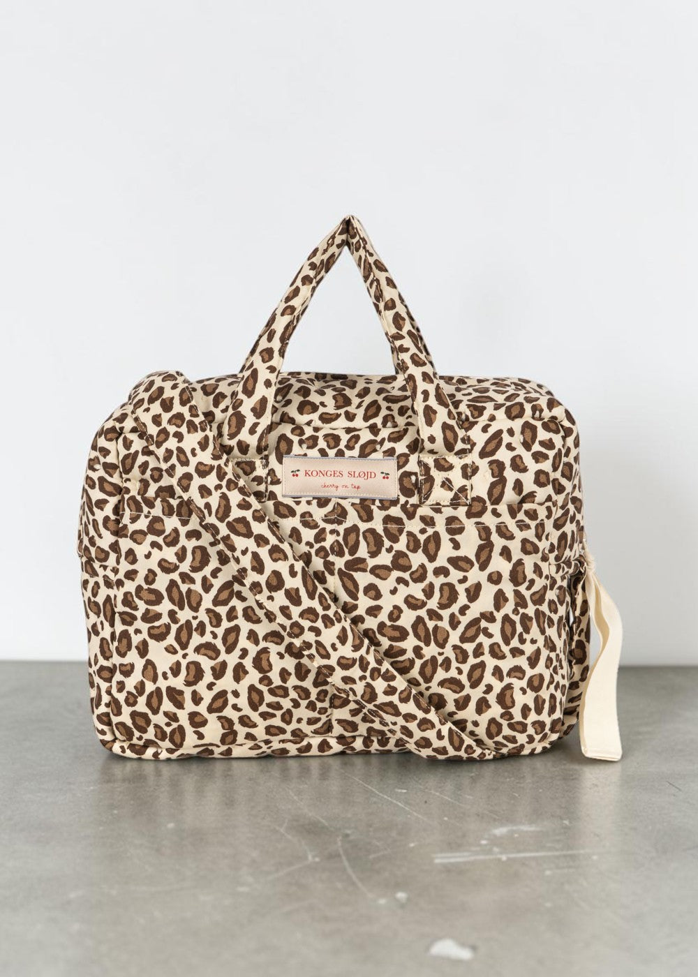 Playroom Collective Konges Sloejd leopard print cotton doll diaper bag with top handles and crossbody strap.