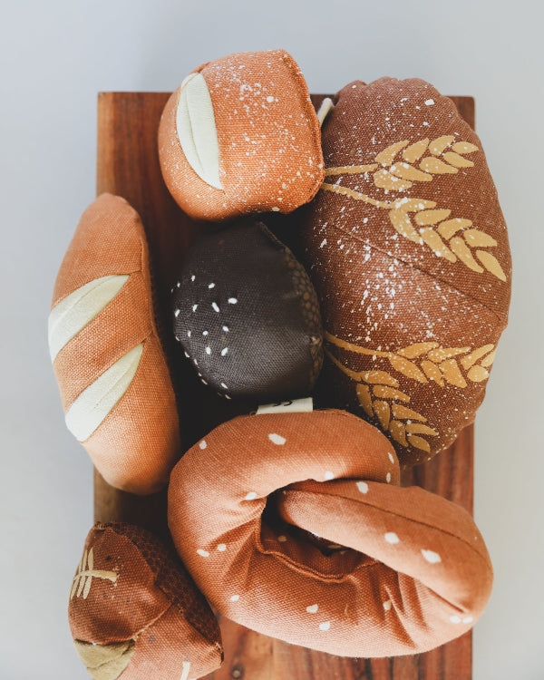 Premium textile play food set showing authentic bread designs with cotton storage bag on wooden cutting board