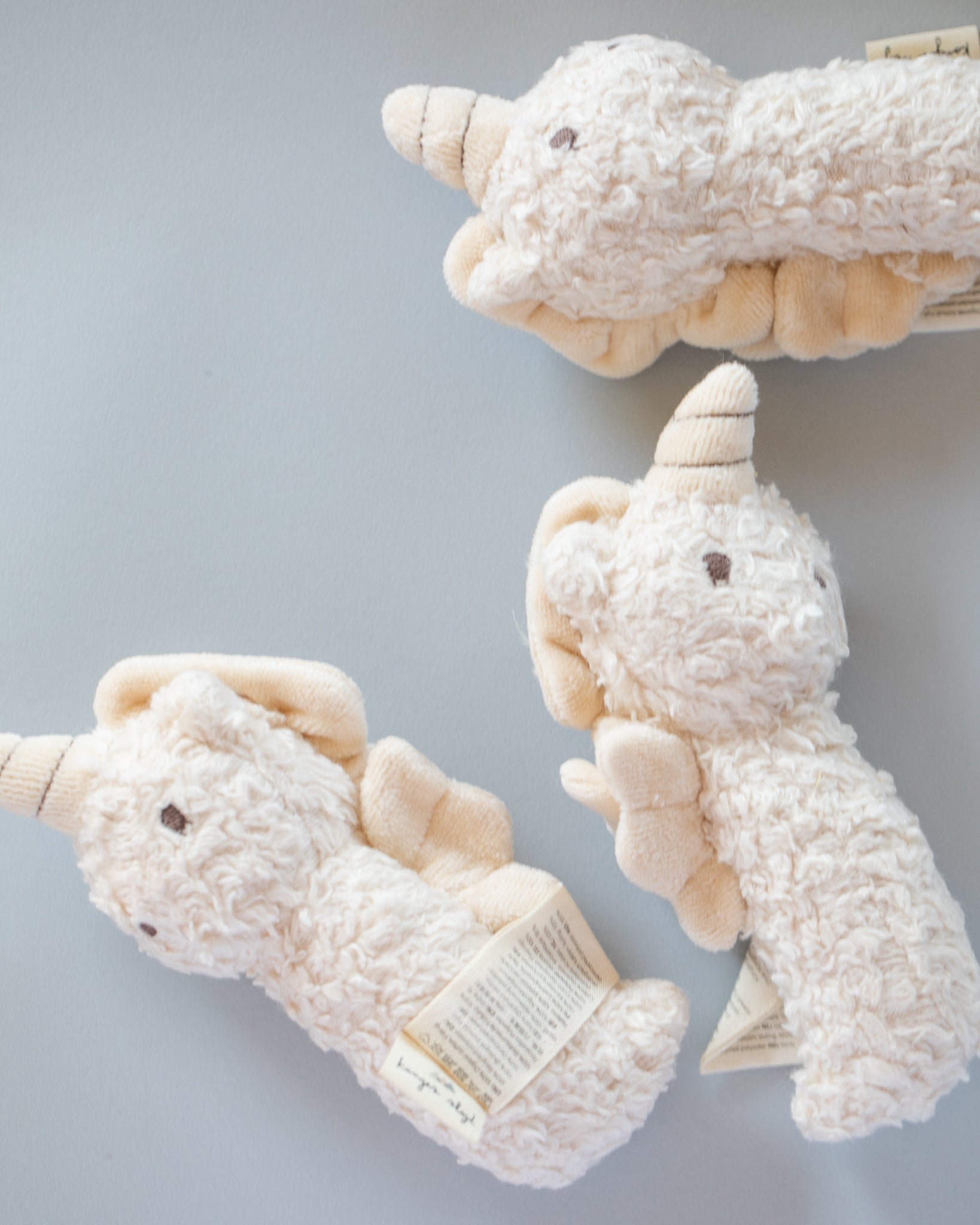 Cream sherpa mini unicorn rattle with organic cotton construction lying on neutral background